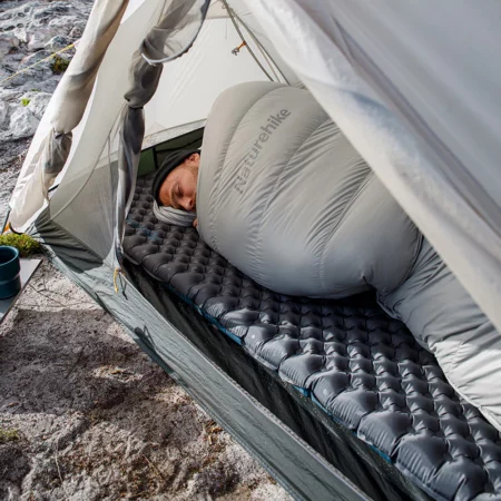 زیرانداز بادی فوق سبک دو نفره نیچرهایک طوسی در چادر که یک مرد در کیسه خواب بر روی آن دراز کشیده است
