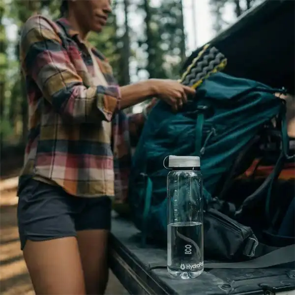 بطری آب HydraPak Recon بر روی پشت یک تراک در کنار یک کوهنورد زن به همراه کوله پشتی با نمایی از جنگل